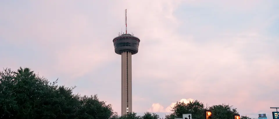 The Tower of the Americas against a pink and blue sky at dusk, above the trees