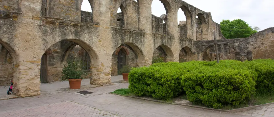 Stone arches of a San Antonio mission's old walls with potted plants and green shrubs below