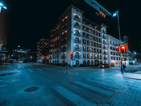 A downtown San Antonio intersection at night, with traffic signals on a mast arm over brick crosswalks and a lit hotel on the corner